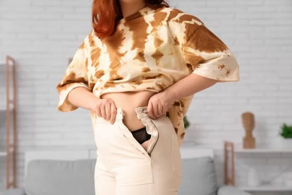 Image of woman trying to do her trousers up after pregnancy weight gain Dunfermline