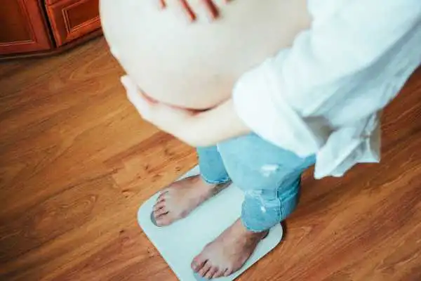 Image of woman weighing herself and experiencing weight gain through pregnancy Dunfermline